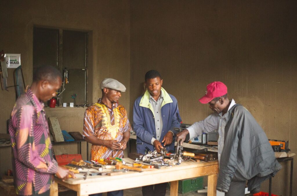 Group of men collaborating in a Ugandan workshop surrounded by tools and equipment.