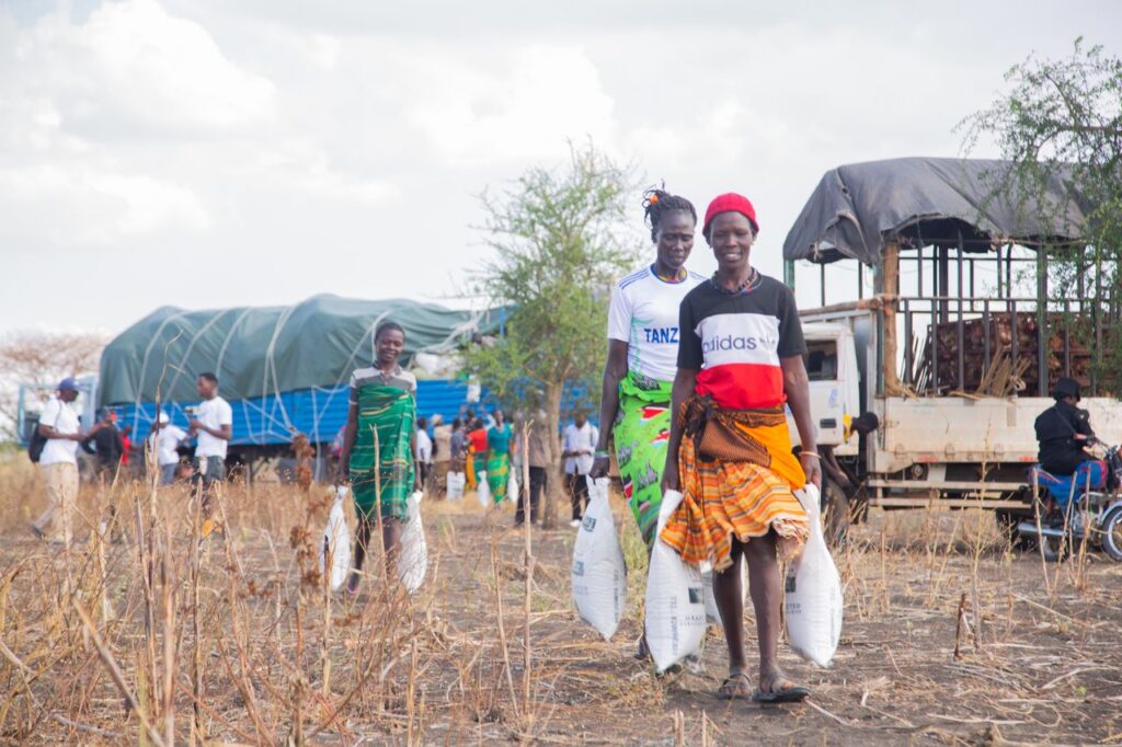 People receiving aid supplies in a rural African community with a truck in the background.