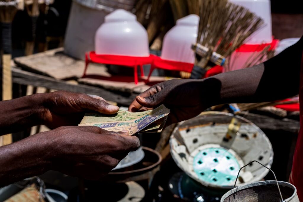 Close-up of hands exchanging Nigerian naira bills at a bustling outdoor market in Nigeria.