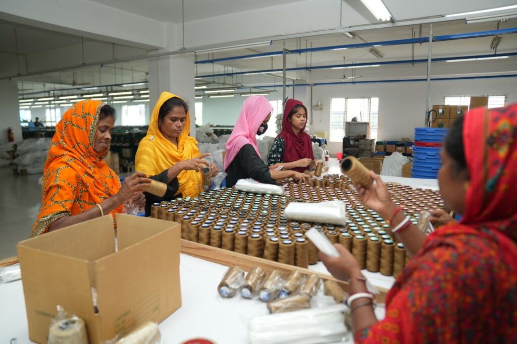 A group of women wearing colorful traditional clothing work together on a textile assembly line in a factory.